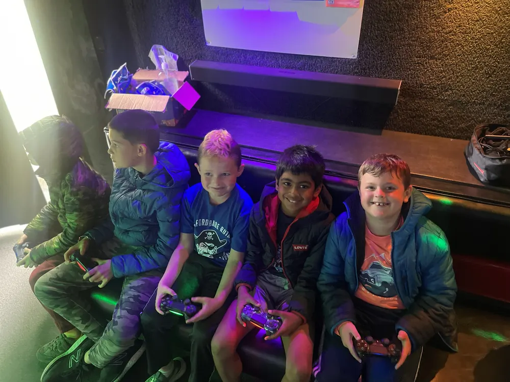 Kids grinning with controllers on the bench inside the game truck at a birthday party